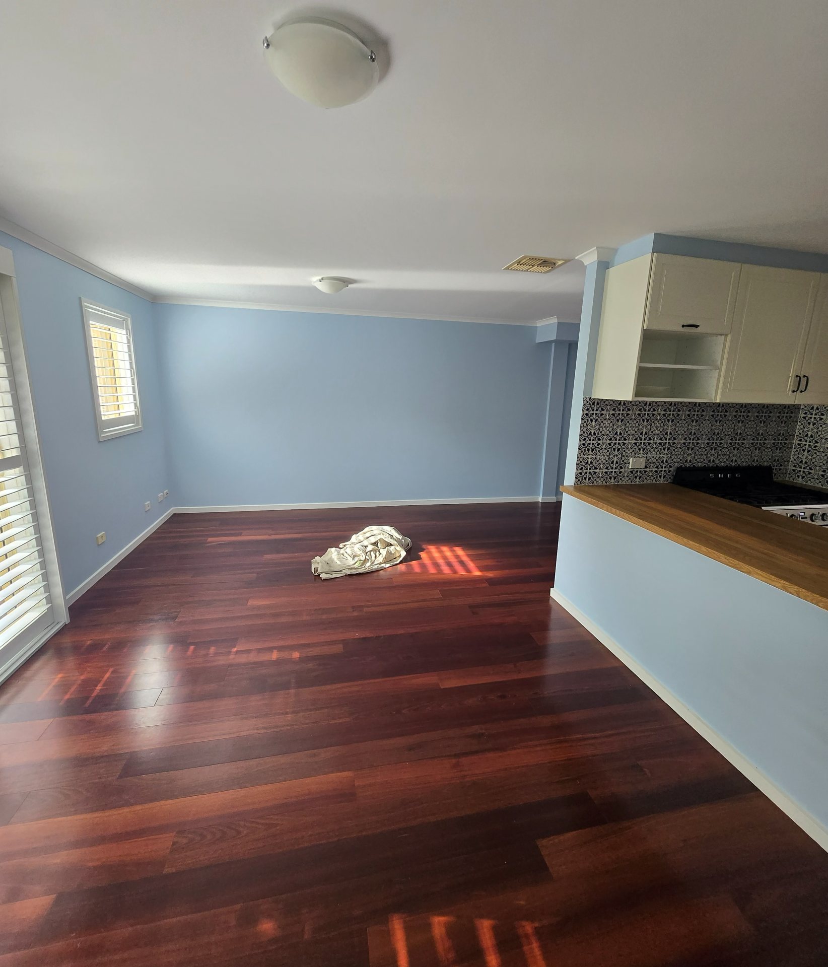 Freshly painted living room with soft blue walls, opening onto a white kitchen